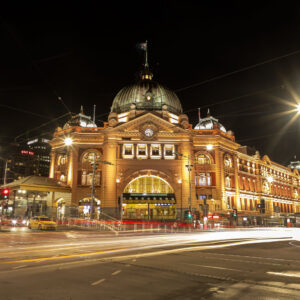A night time photo of Flinders street station with light trails caused by long exposures from passing trams