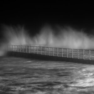 Black and White photo of ocean waves hitting a pool wall at night